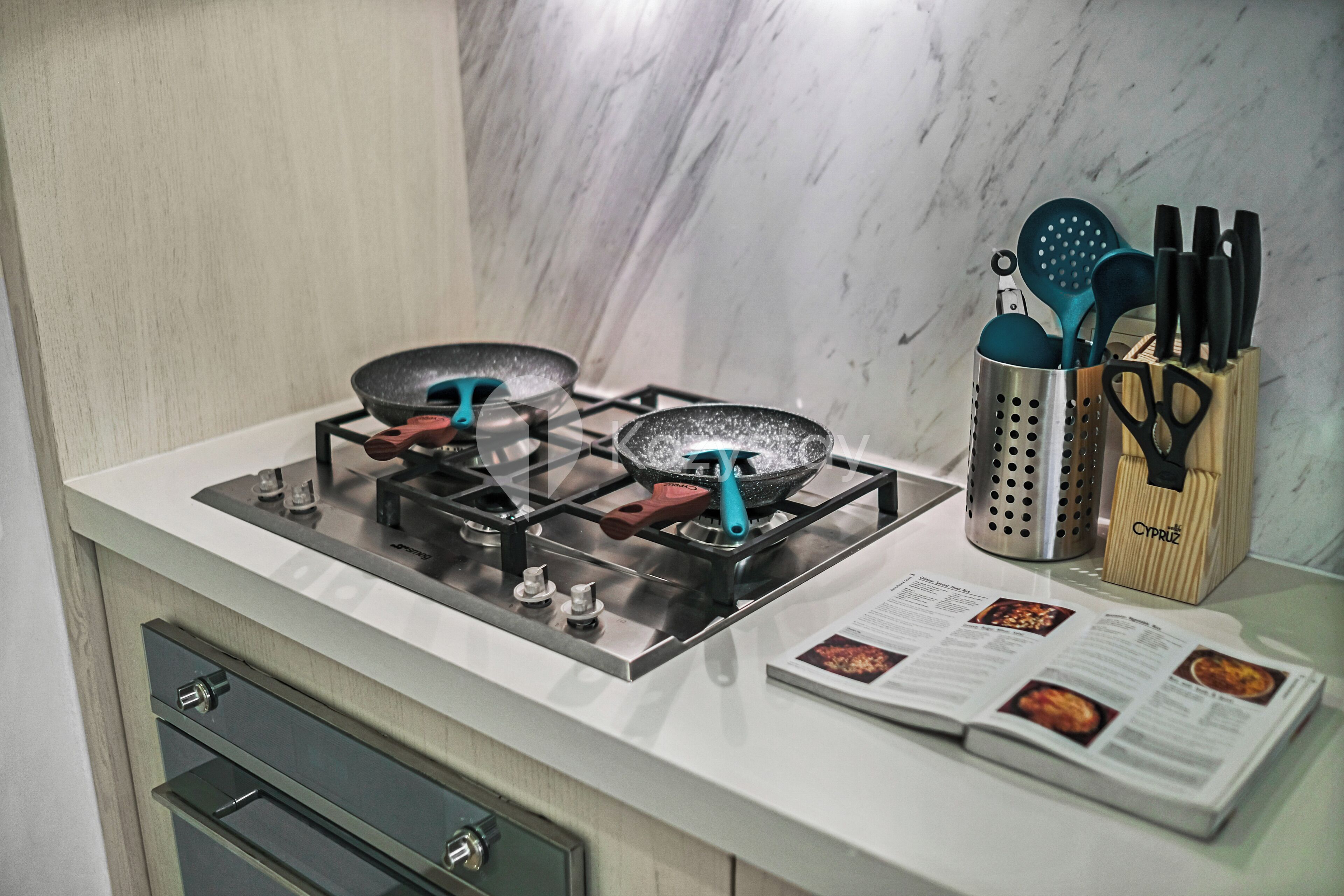 A kitchen with a gas stove, a cookbook, and a utensil holder.