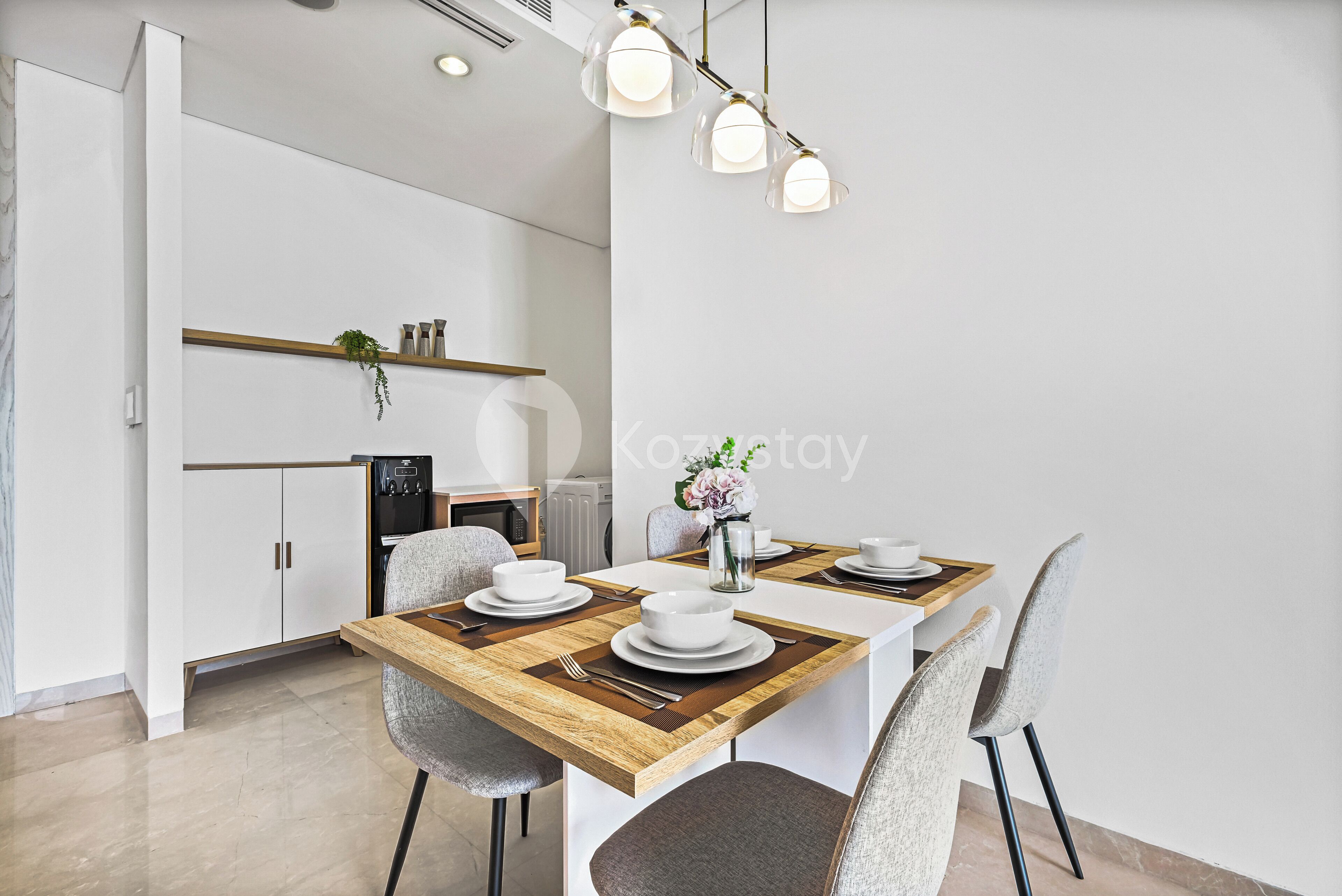 Un espace de salle à manger moderne avec une table en bois, des chaises à revêtement gris et des luminaires suspendus.