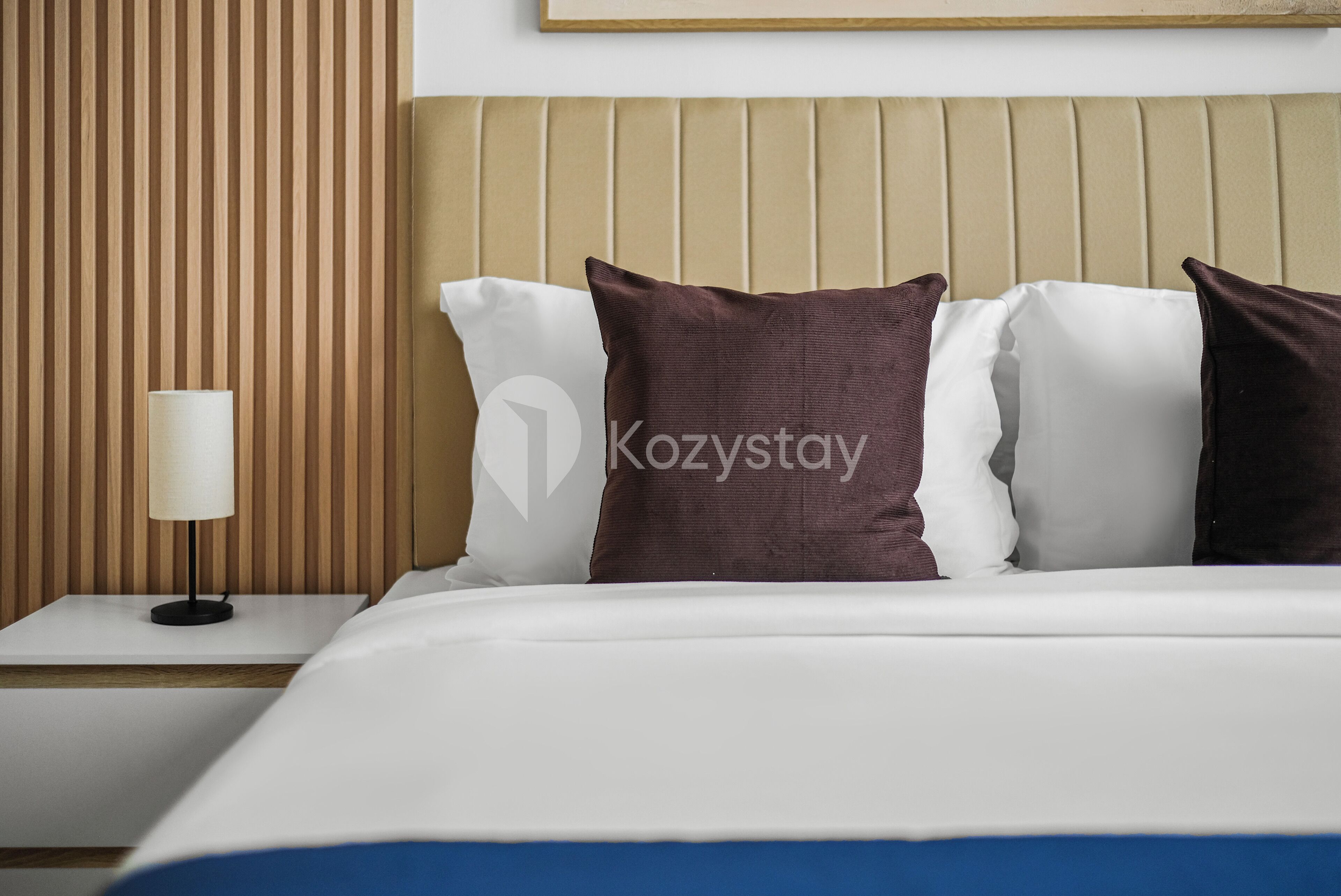 A hotel room with a bed, pillows, a nightstand, and a lamp.