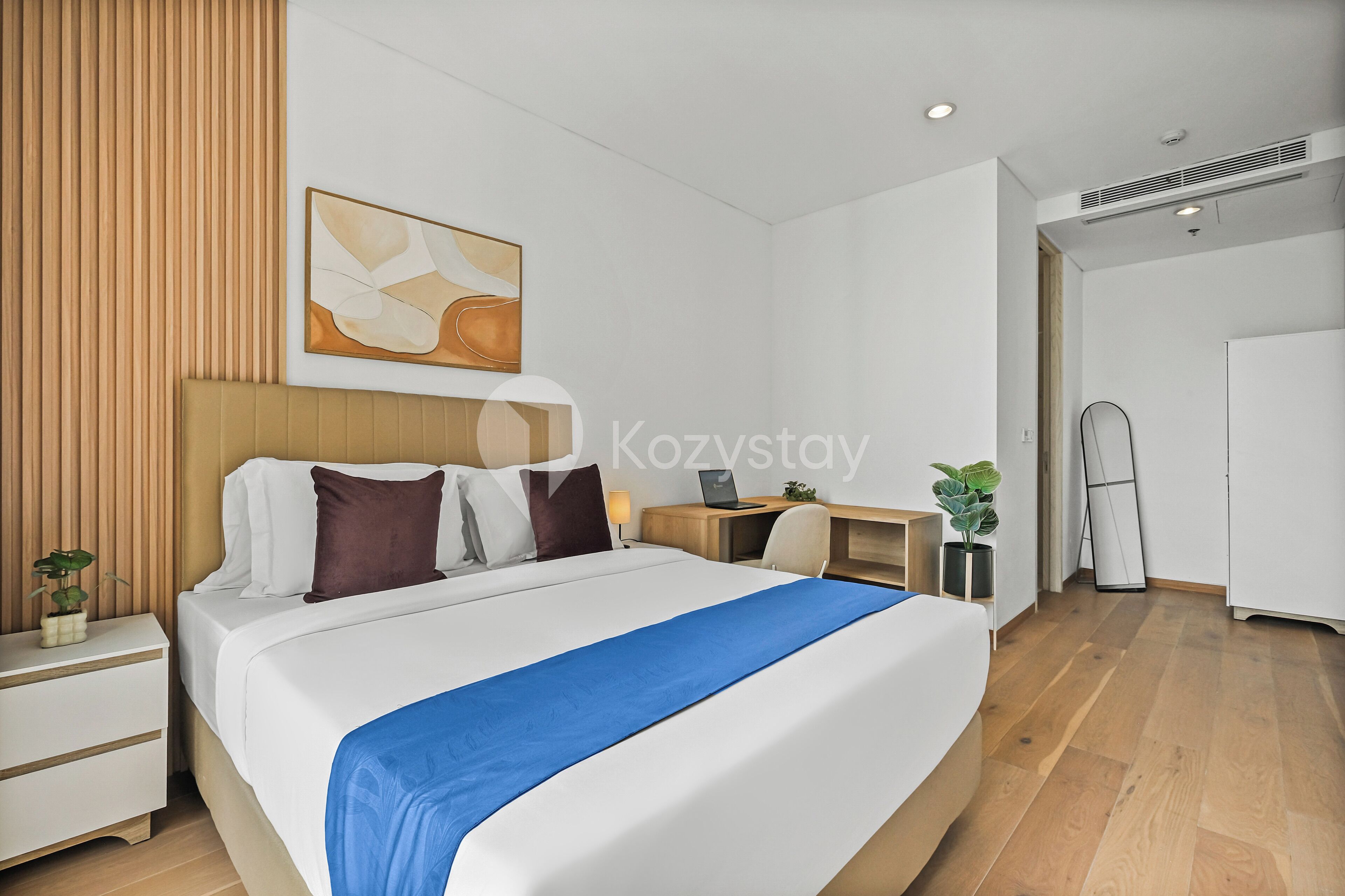 Ein modernes Hotelzimmer mit einem großen Bett, einem Schreibtisch, einem Laptop und einer Zimmerpflanze.
