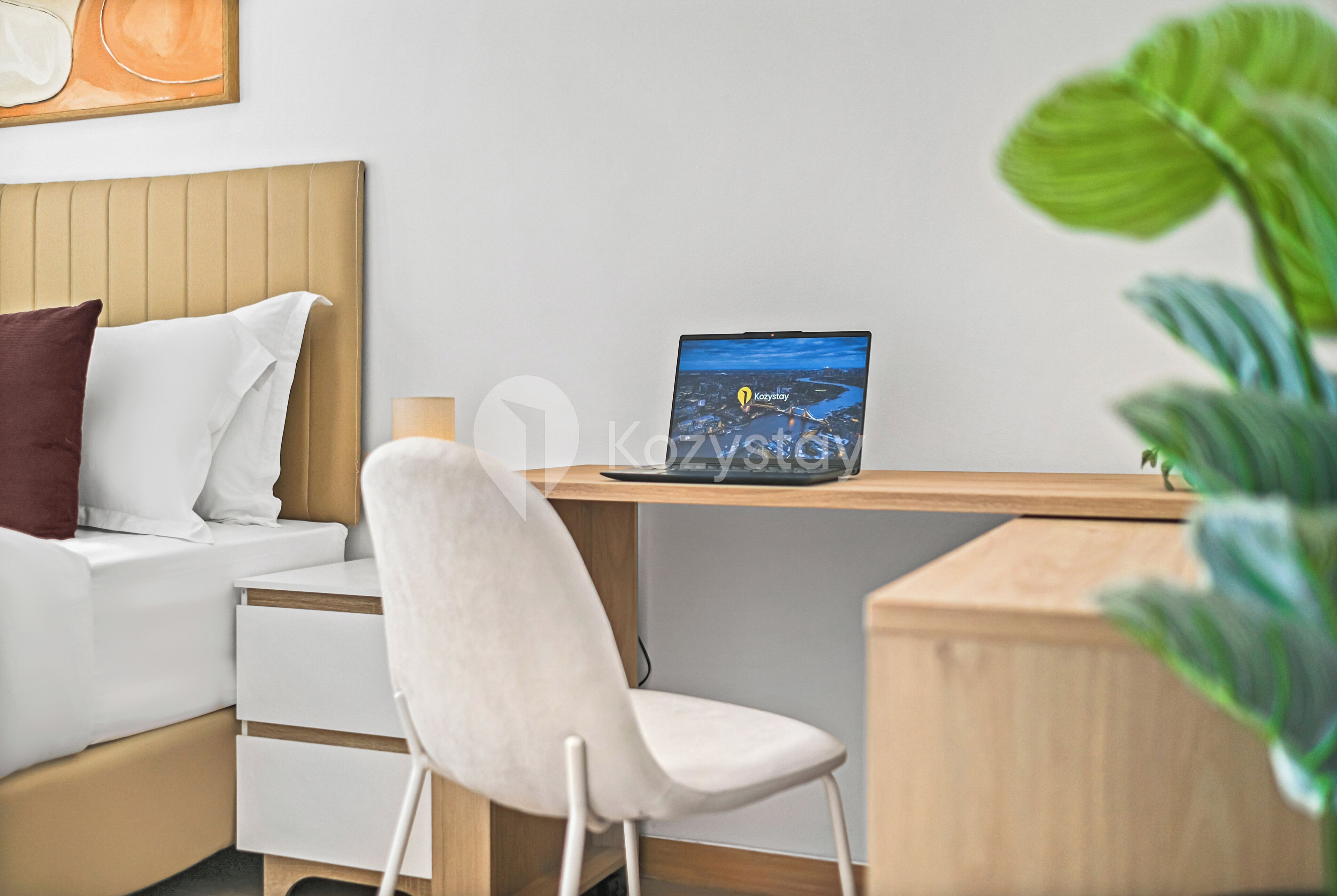 Egy modern hálószoba, amelyben található egy ágy, egy éjjeliszekrény, egy szék, és egy laptop, amelyen egy városi panoráma látható.