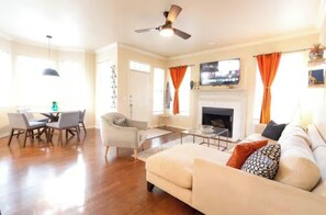 A spacious living room with a fireplace, a dining area with a table and chairs, and a sofa with decorative pillows. - Luxury Condo - Prime Location -Ideal Mid-term Rental (Rogers)