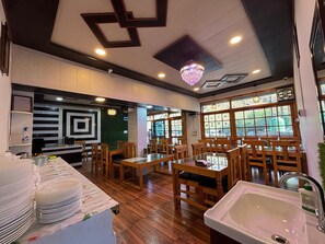 Un restaurante con mesas y sillas de madera, una mesa de comedor con superficie de vidrio y un lavabo.