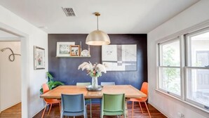 Een eetgedeelte met een houten tafel, stoelen, een hanglamp en kunst aan de muur.