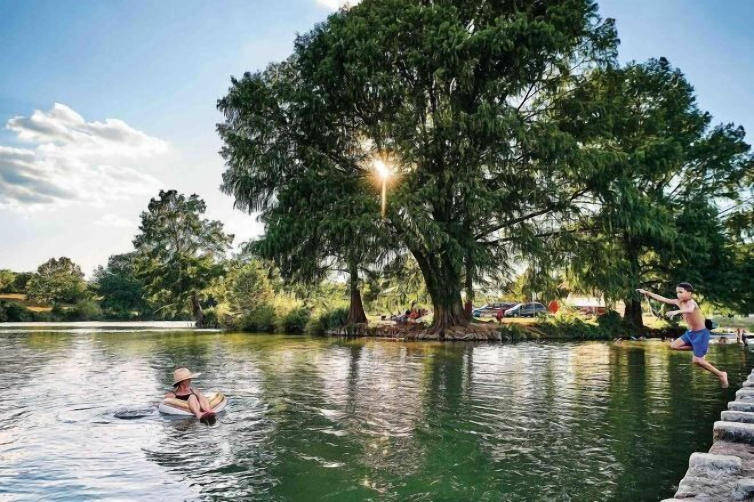 A lake with a person in a boat and another person jumping into the water.