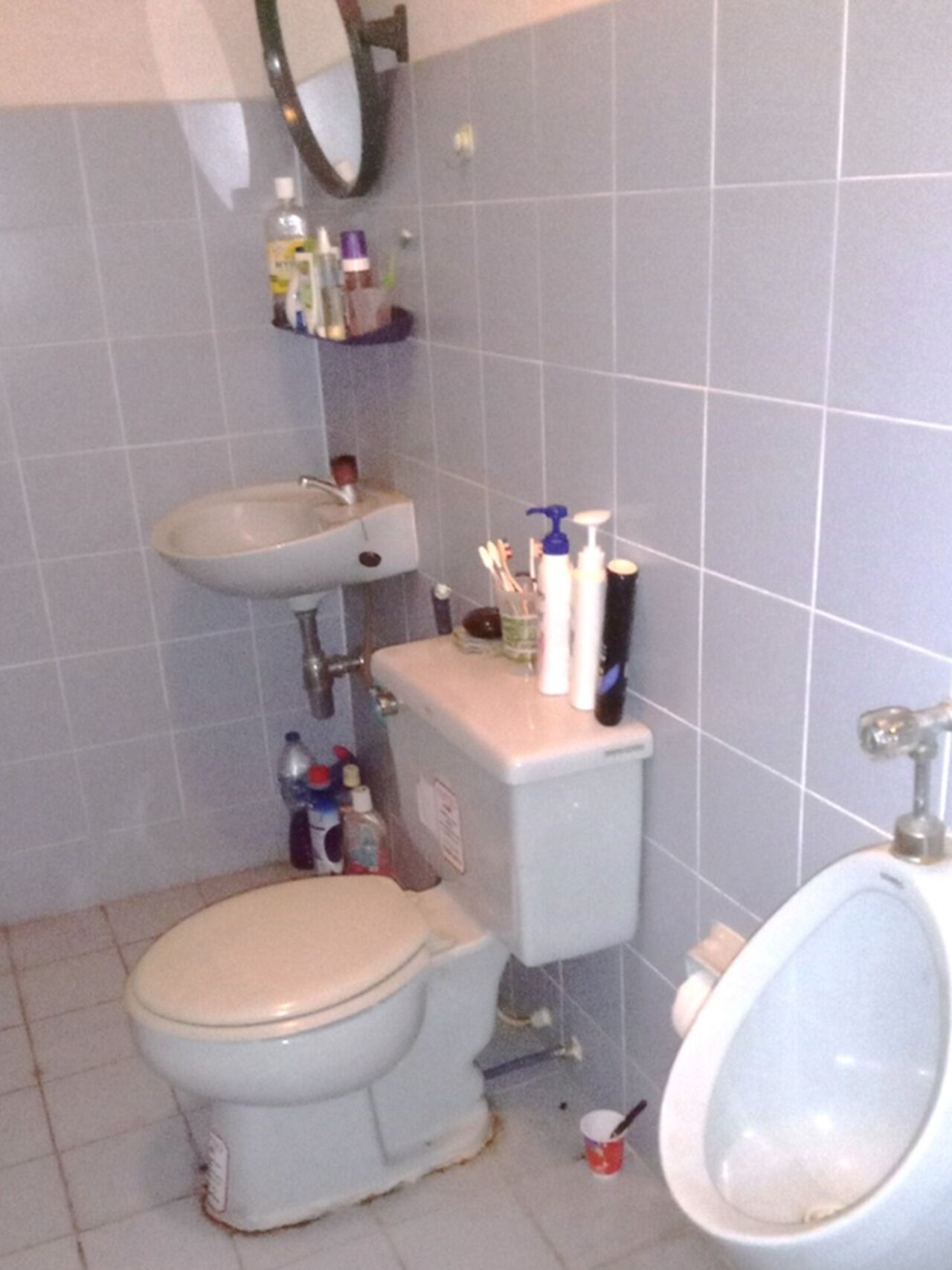 A small bathroom with a toilet, sink, and bidet. There are toiletries on the sink and toilet.