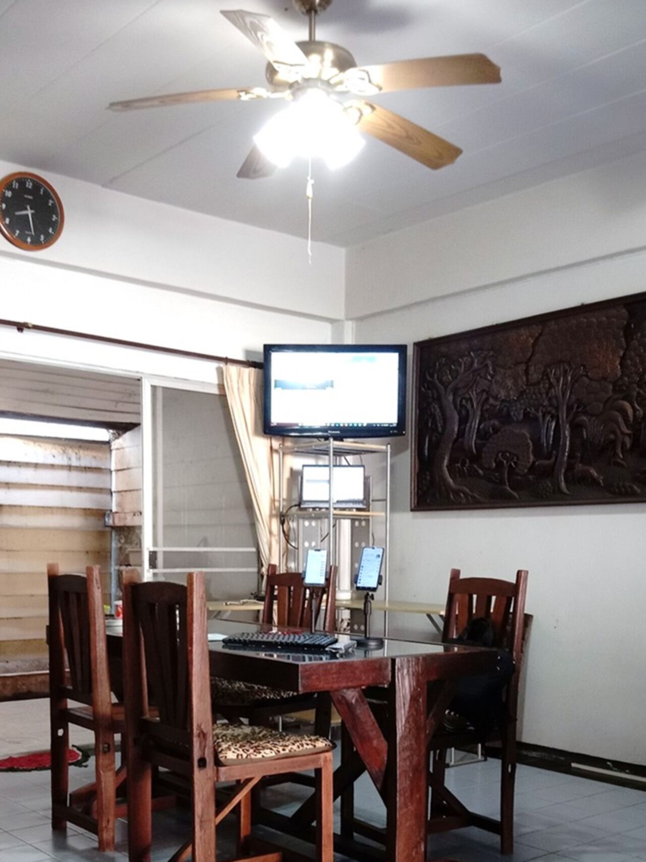 A dining area with a ceiling fan, a clock, a television, and a decorative wall piece.