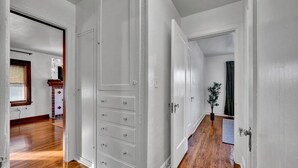 En hall med vita väggar och trägolv, som leder in till ett rum med en stor, vit garderob och en liten växt.