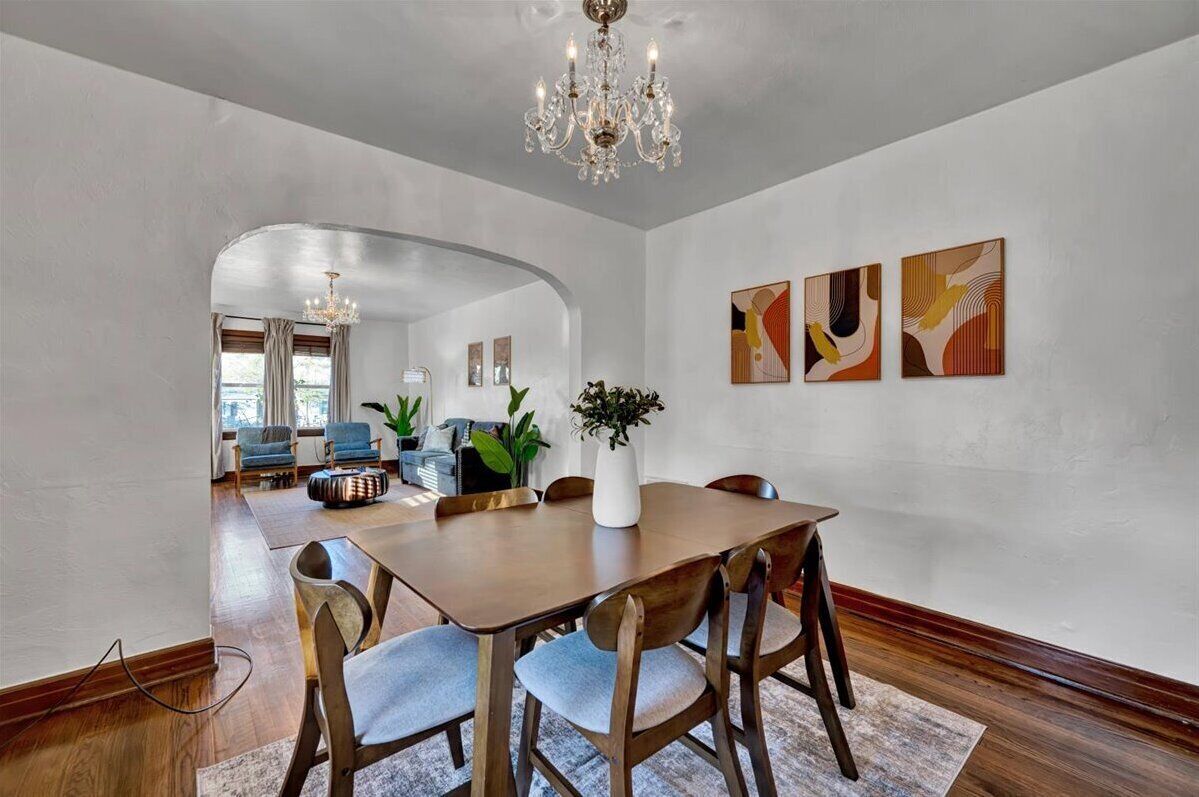 A dining area with a wooden table and chairs, a chandelier, and abstract art on the wall.