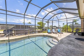 An indoor swimming pool with a glass ceiling, a barbecue area, and a seating area with chairs. - Reel Serenity (Cape Coral)