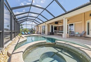 A pool with a glass enclosure, outdoor furniture, and a covered patio area. - Reel Serenity (Cape Coral)