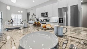 Una cocina moderna con encimera de mármol, electrodomésticos de acero inoxidable y un comedor con un plato, taza y utensilios.