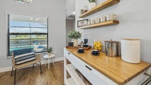 Una cocina moderna con mostradores de madera, armarios blancos y una unidad de estanterías empotradas que exhibe utensilios de cocina y plantas.