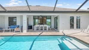 Una casa moderna con piscina, un porche cubierto con mobiliario exterior y ventanas amplias.