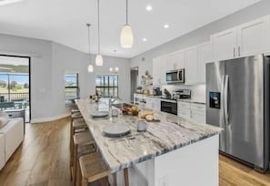 A modern kitchen with a marble countertop, stainless steel appliances, and a large island with seating. - Sun Soaked (Cape Coral)