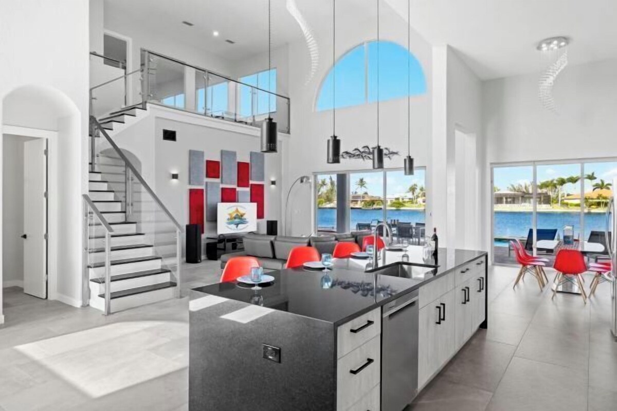 A modern kitchen with a central island, a staircase, and a view of the ocean.