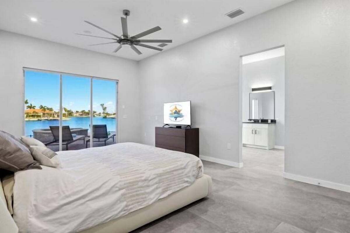 A bedroom with a bed, a ceiling fan, a TV, and a view of a pool.