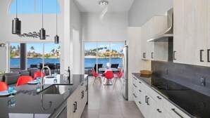 Una cucina moderna con isola centrale, zona pranzo con sedie rosse e vista sull'oceano.