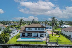 A two-story house with a swimming pool, surrounded by a well-maintained lawn and palm trees. - Villa Stella (Cape Coral)