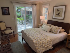 A bedroom with a bed, a chair, a nightstand, a lamp, a window, and a door leading to a patio.