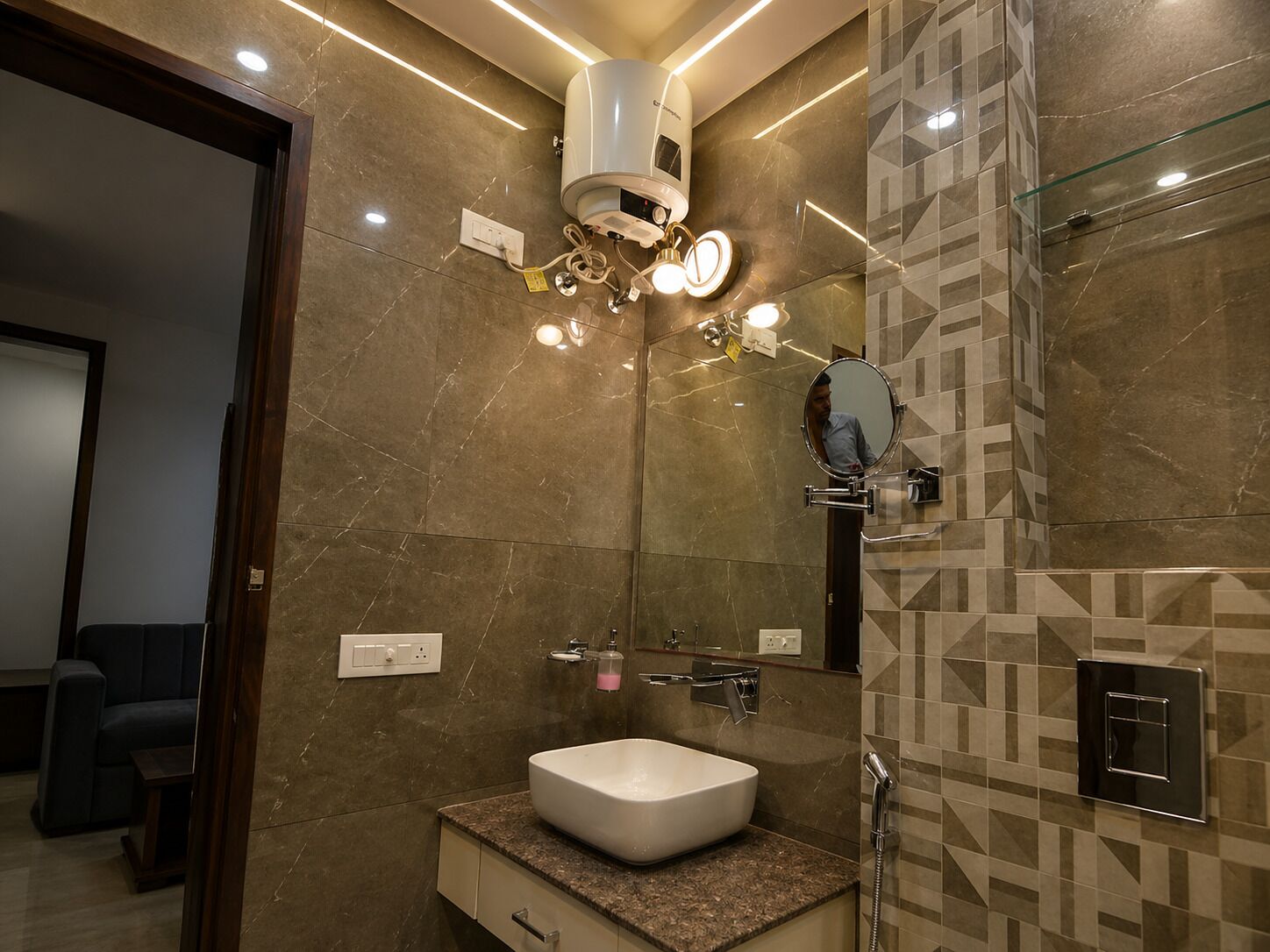 A modern bathroom with a marble wall, a white sink, a mirror, and a handheld showerhead.