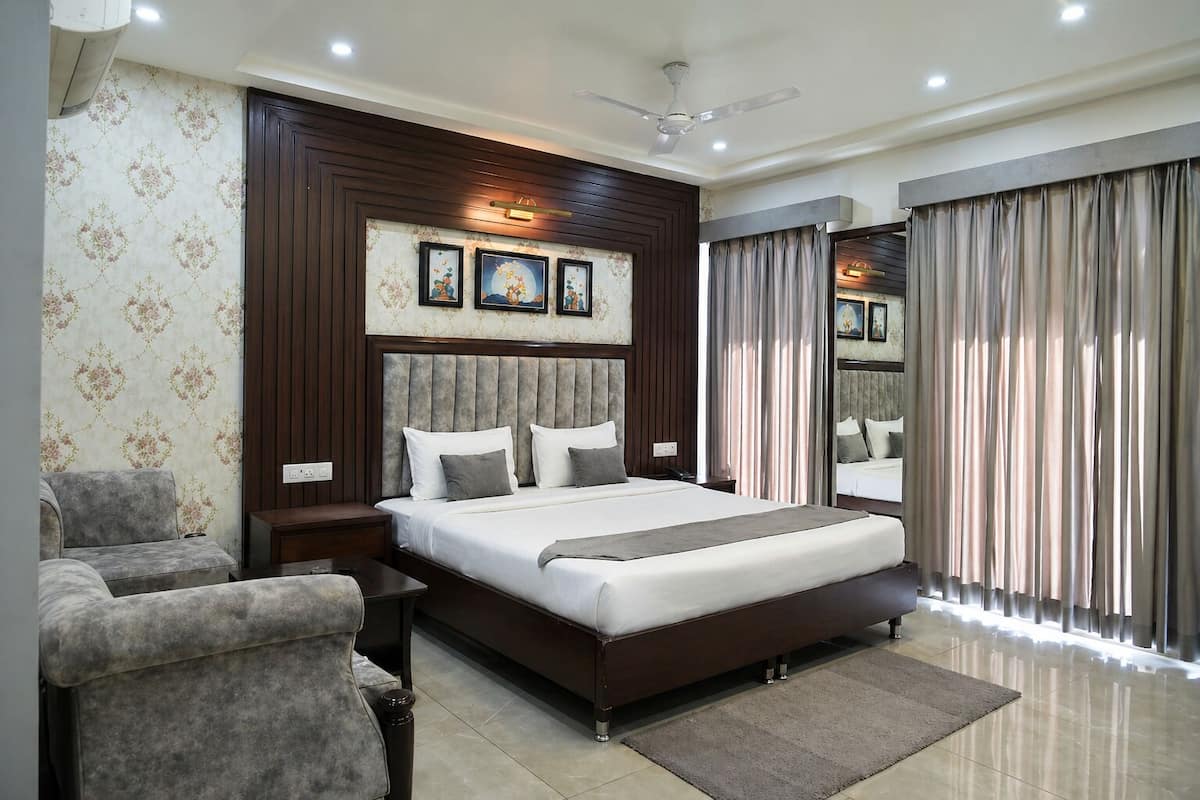 A modern hotel room with a large bed, a sofa, a bedside table, a ceiling fan, and a large window with curtains.