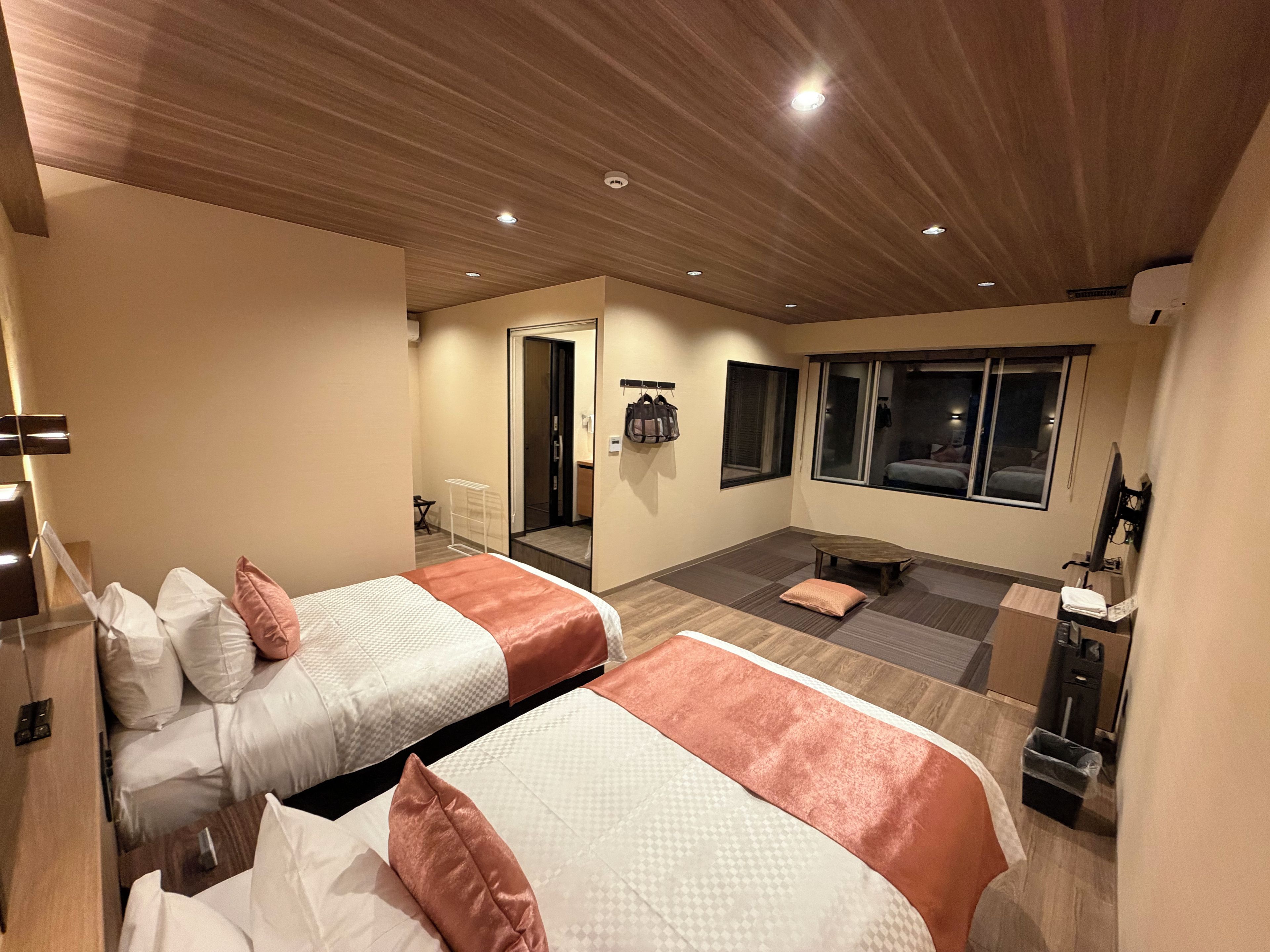 A hotel room with two beds, a sitting area, a TV, and a window.