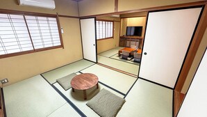 A traditional Japanese room with tatami flooring, a tatami mat table, a tatami mat cushion, a television, and a sliding door. - Livemax Resort HidaTakayama GaryunoSato (Takayama)