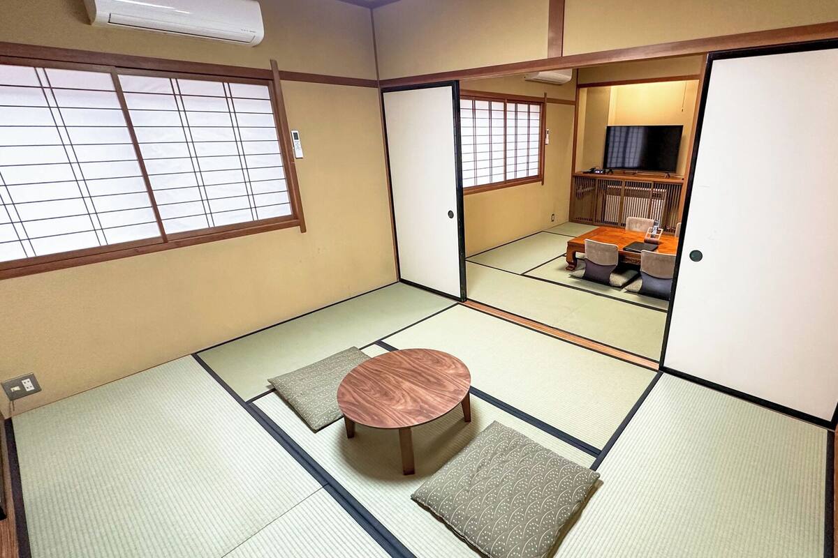 Una habitación tradicional japonesa con suelo de tatami, una mesa baja de tatami y un cojín de tatami, una televisión y una puerta corredera.