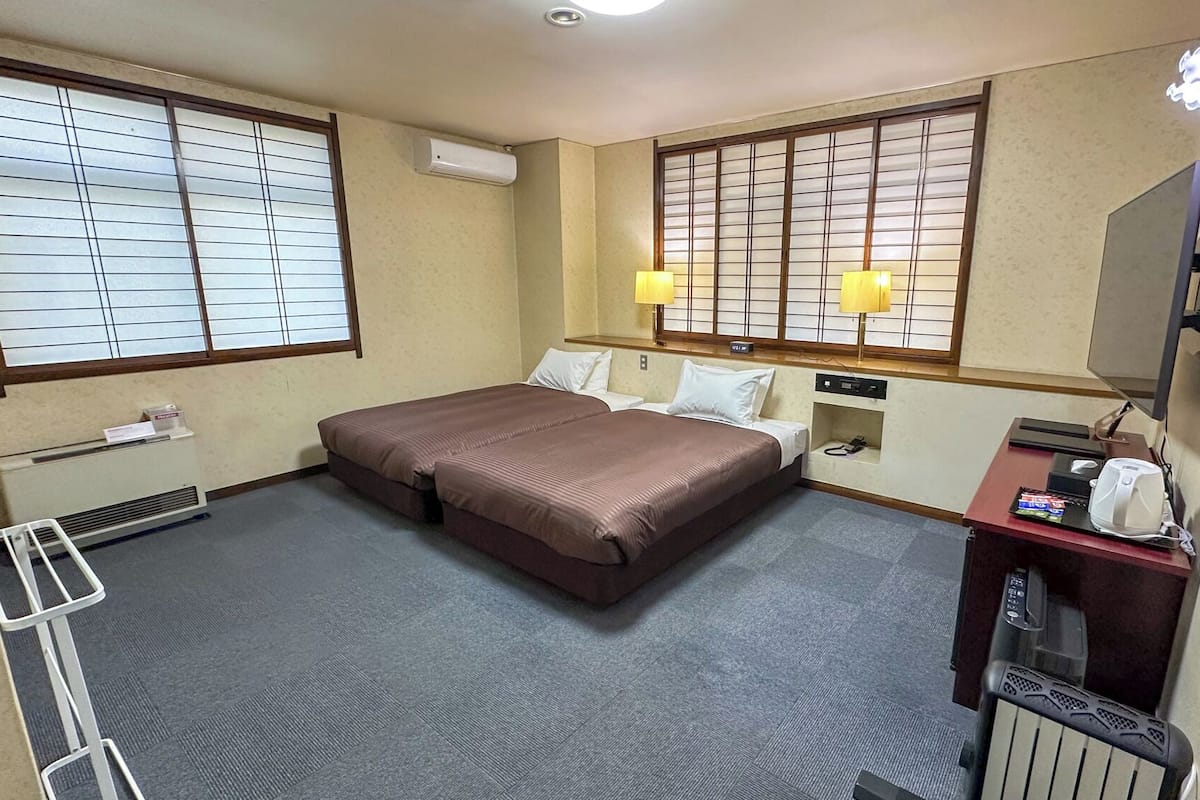 Habitación de hotel con dos camas, un escritorio con computadora y cafetera, un espejo y una ventana con persianas.