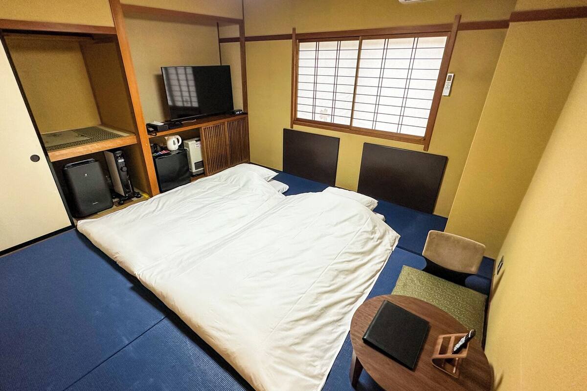 Una habitación pequeña con cama, escritorio, televisor y ventana con diseño de celosías.