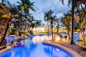 A resort with a large pool surrounded by rocks and palm trees, and a building with a poolside area in the background. - Modern Coastal Home in Reef Resort Port Douglas with Pool Access | Havenwood Townhouse (Port Douglas)