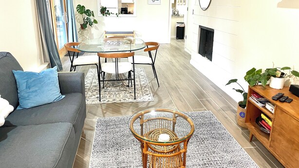 Una sala de estar moderna con un sofá gris, una mesa de centro de vidrio, una mesita de mimbre y una chimenea.