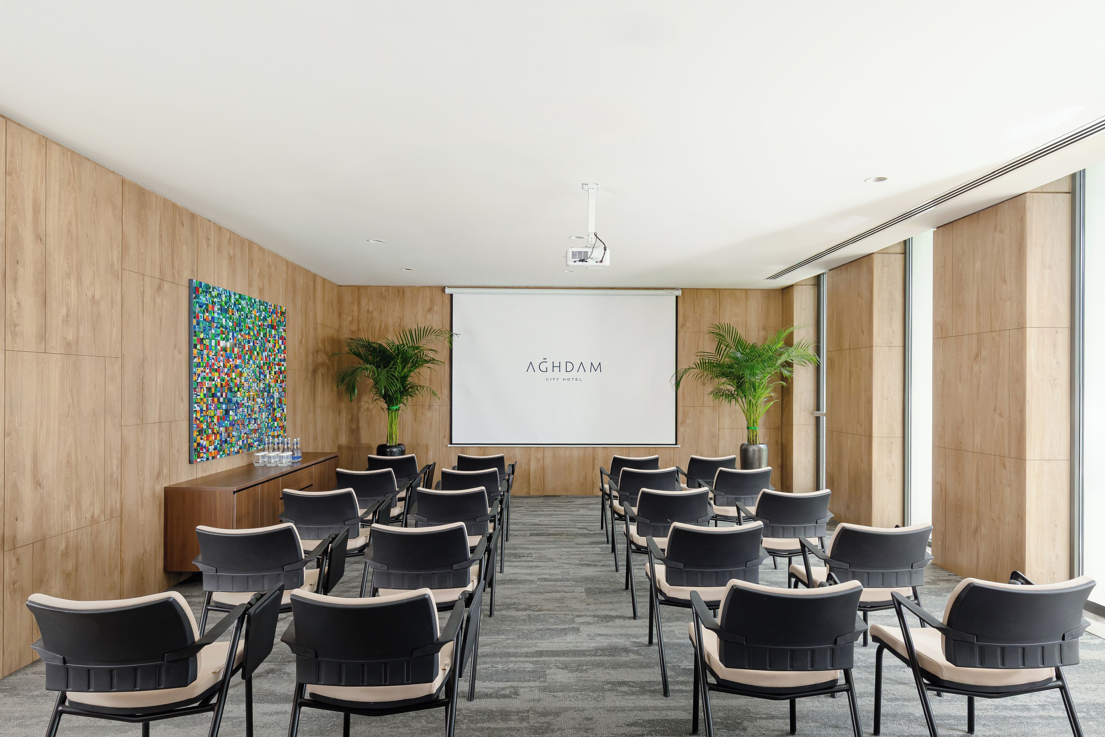 A conference room with a projector screen, a colorful abstract painting, and potted plants.