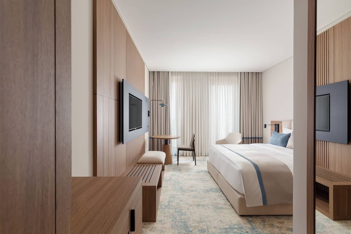 Une chambre d’hôtel moderne avec un grand lit, un bureau et un téléviseur fixé au mur.