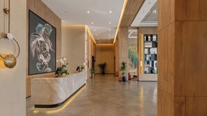 A modern reception area with a marble counter, a large abstract painting, and potted plants. - Aghdam City Hotel (Aghdam)
