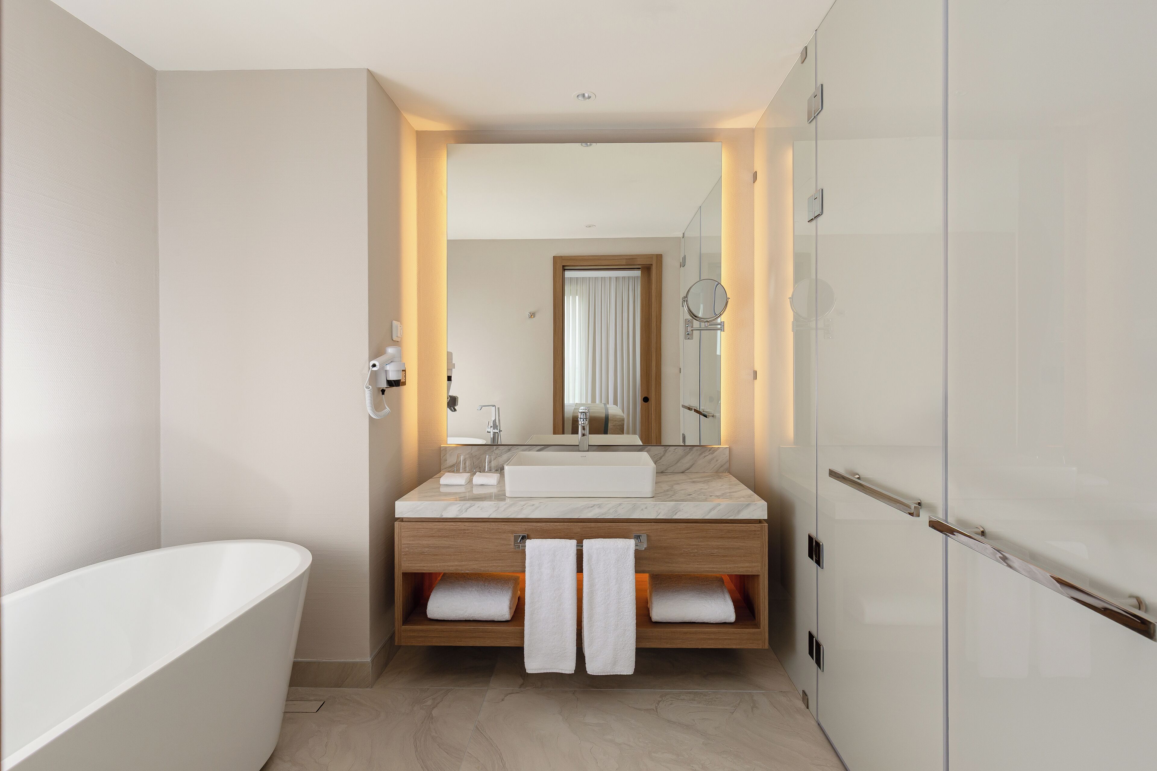 A modern bathroom with a freestanding bathtub, a large mirror, and a vanity with a sink and towel racks.