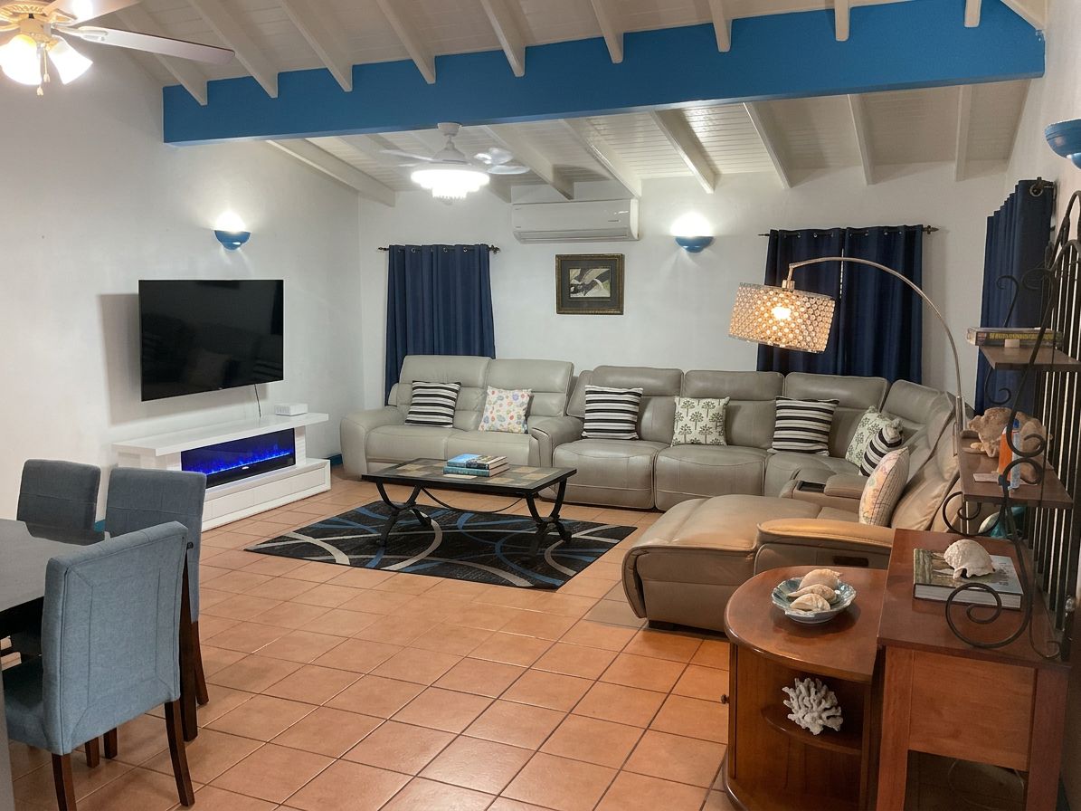 A living room with a sofa set, a flat-screen TV, a dining area with chairs, and a coffee table.