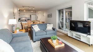 A modern living room with a grey sofa, a coffee table with a plant, and a TV on a white stand. - Whistler Village Stroll Condo with AC and Free Parking (Whistler)