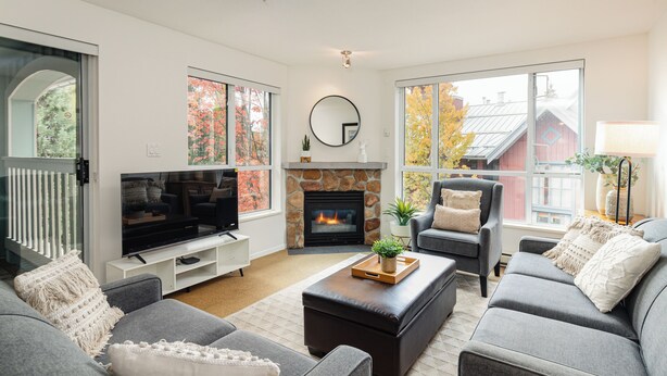 A modern living room with a fireplace, large windows, and a television. - Whistler Village Stroll Condo with AC and Free Parking (Whistler)