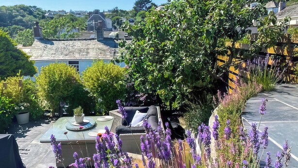 Een dakbalkon met zitplaatsen, plantenpotten en uitzicht op de omgeving.