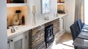 Een moderne keuken met een stenen open haard, witte kasten en een eethoek met een tafel en stoelen.