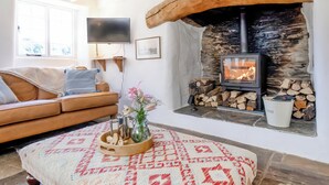 A cozy living room with a stone fireplace, a sofa, a TV, and a decorative table with a rug. - 4 bedroom accommodation in Portscatho (Portscatho)