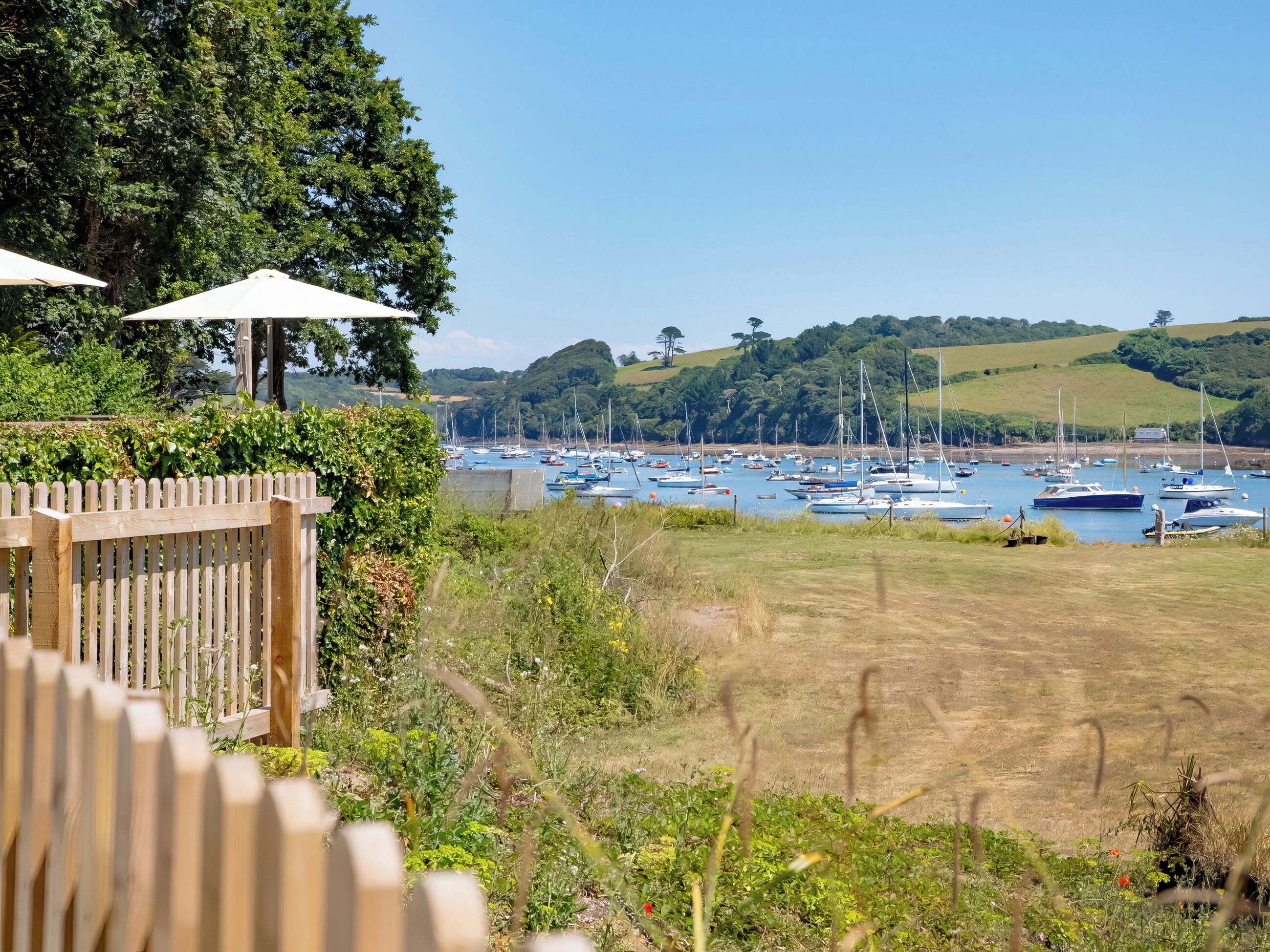 A marina with multiple boats docked, surrounded by greenery and hills.