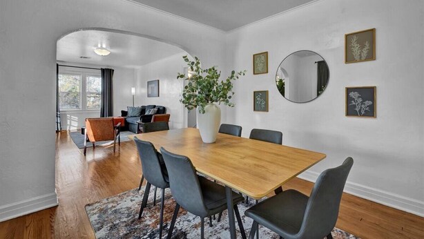 Een eetgedeelte met een houten tafel, zwarte stoelen, een witte vaas met groen en lijstwerken aan de muren.