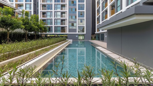 Um edifício moderno com piscina, rodeado por vegetação e com varandas com guarda-corpos de madeira.
