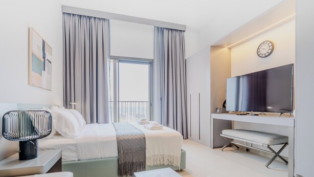 Habitación de hotel moderna con cama, mesita de noche, lámpara, televisor y escritorio con silla.