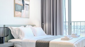 Una cama bien hecha con sábanas blancas, un edredón gris y toallas enrolladas al lado.