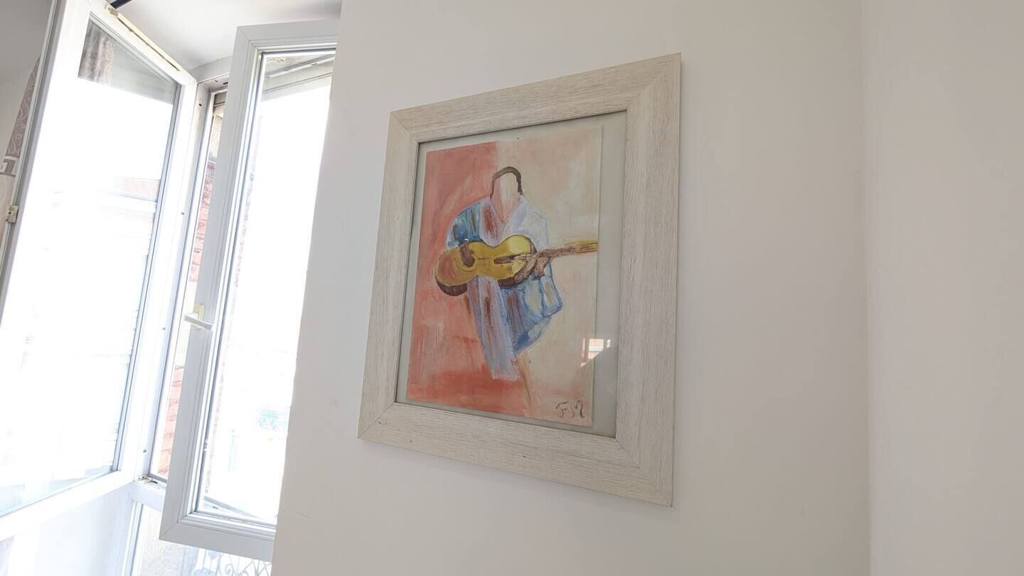 A framed artwork of a person playing a guitar on a white wall.