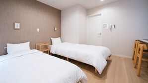 A hotel room with two beds, a wooden nightstand, a desk with a chair, and a door. - TEN6-TenSix- (Osaka)